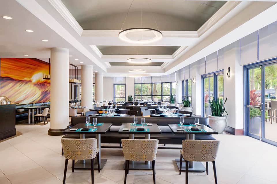 Modern dining room with black tables, beige chairs, and floor-to-ceiling windows with bright natural light