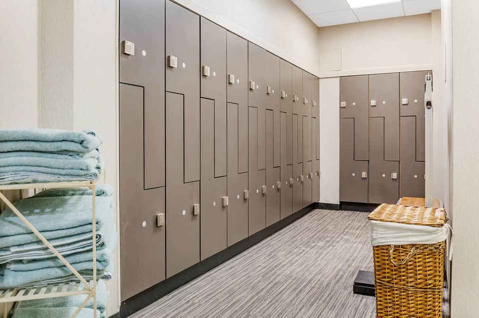 Locker room with rows of brown lockers, shelves with folded towels, and baskets