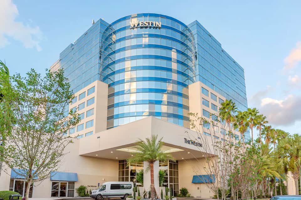 Modern blue and white Westin hotel building exterior with curved glass architecture and palm trees