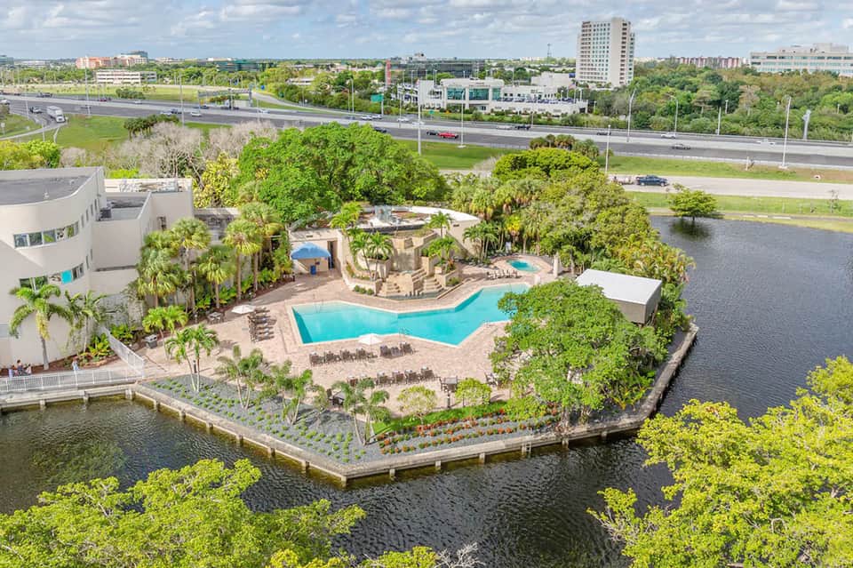 Aerial view of waterfront resort pool surrounded by palm trees and tropical landscaping