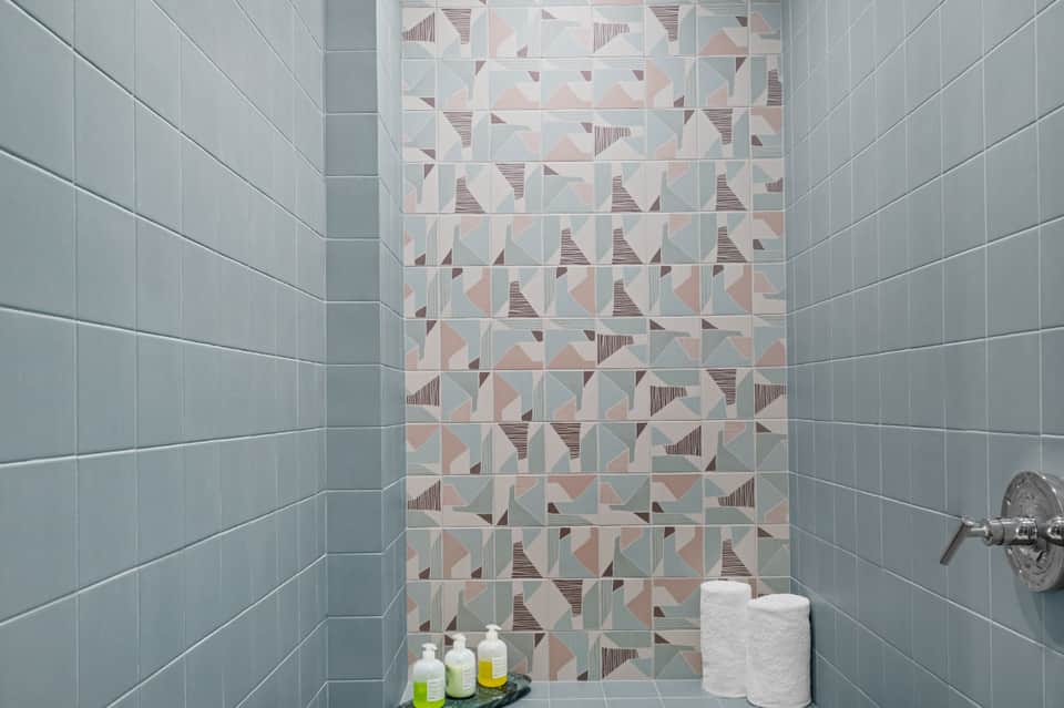 Bathroom shower with geometric patterned tile wall in teal, beige, and coral tones with chrome fixtures