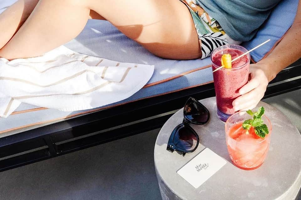 Overhead view of two people lounging by pool with colorful cocktails and sunglasses