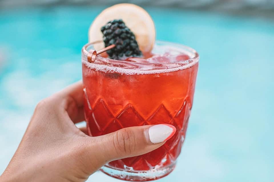 Red cocktail with sugared rim and lychee garnish by a turquoise swimming pool