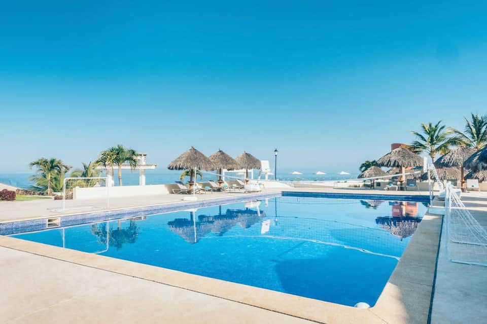Resort infinity pool overlooking turquoise ocean with thatched umbrellas and white loungers