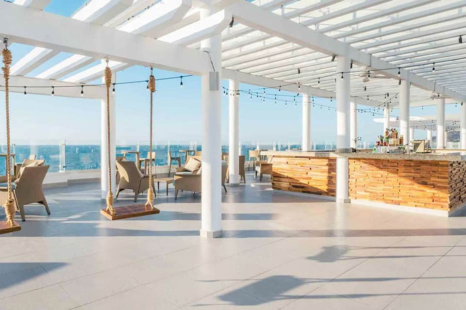 Bright white pergola structure with rope swings, wooden bars, and expansive ocean view from deck
