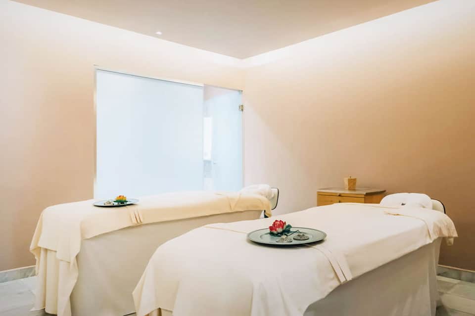 Spa treatment room with two massage tables, cream linens, large window, minimalist decor