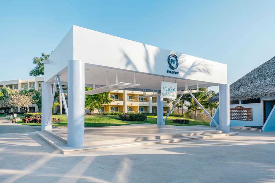 White modern yoga pavilion with X-braced columns and palm trees in tropical resort setting