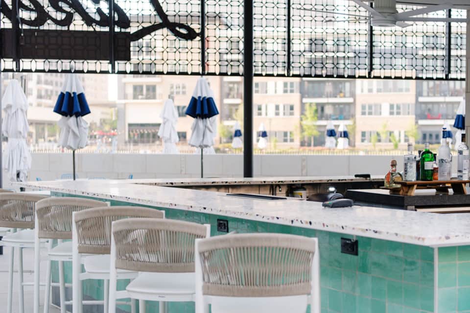 Modern rooftop bar with white barstool seating, turquoise accents, and city skyline views