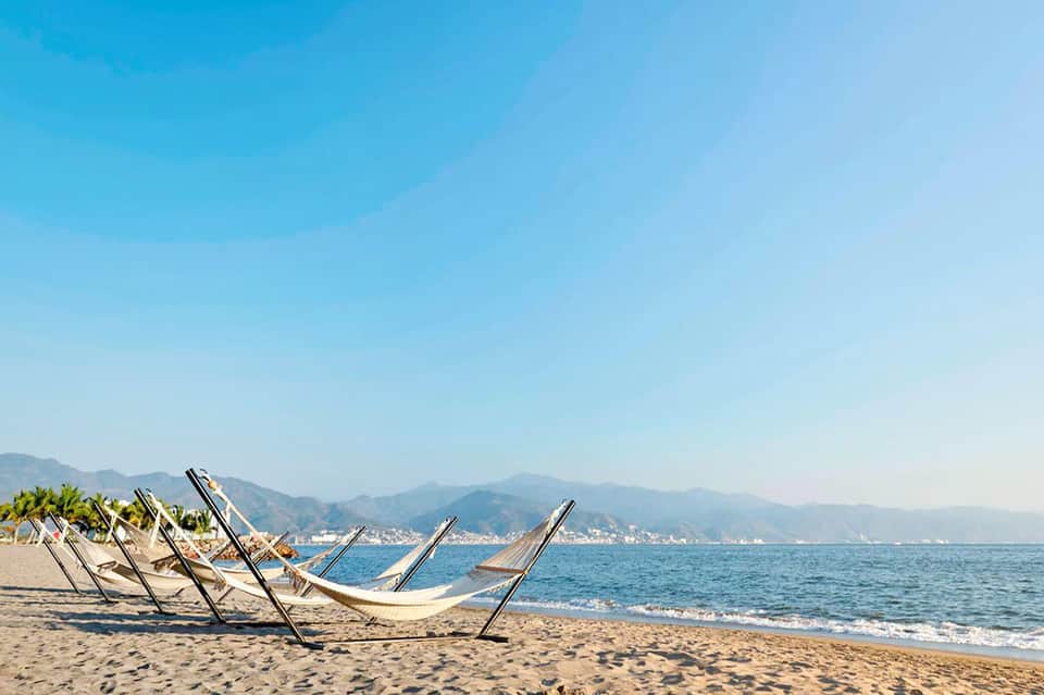 Empty beach loungers facing the ocean with mountains and coastal town in the background