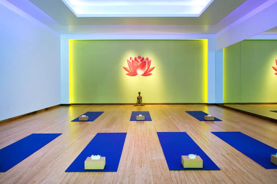 Modern yoga studio with blue mats, illuminated lotus flower artwork, and wooden flooring