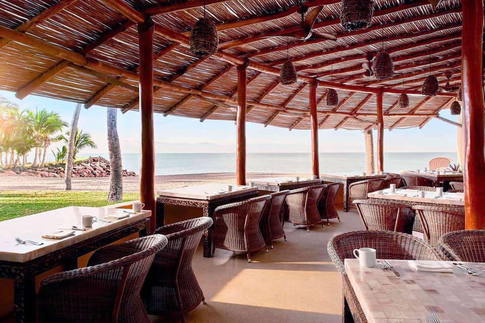 Beachfront dining area with wooden pergola, wicker chairs, and ocean views