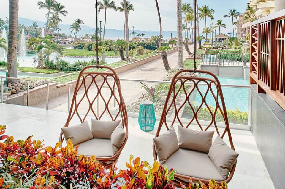 Two woven hanging chairs with cushions overlooking tropical resort grounds and golf course