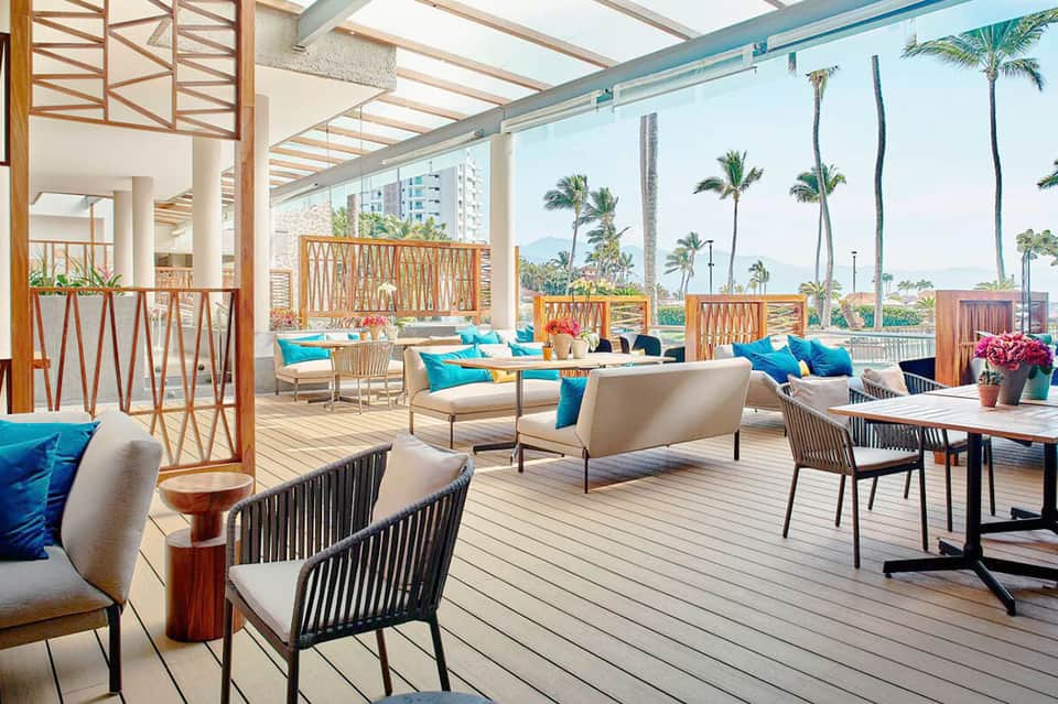 Modern rooftop lounge with palm trees, turquoise cushions, and mountain views