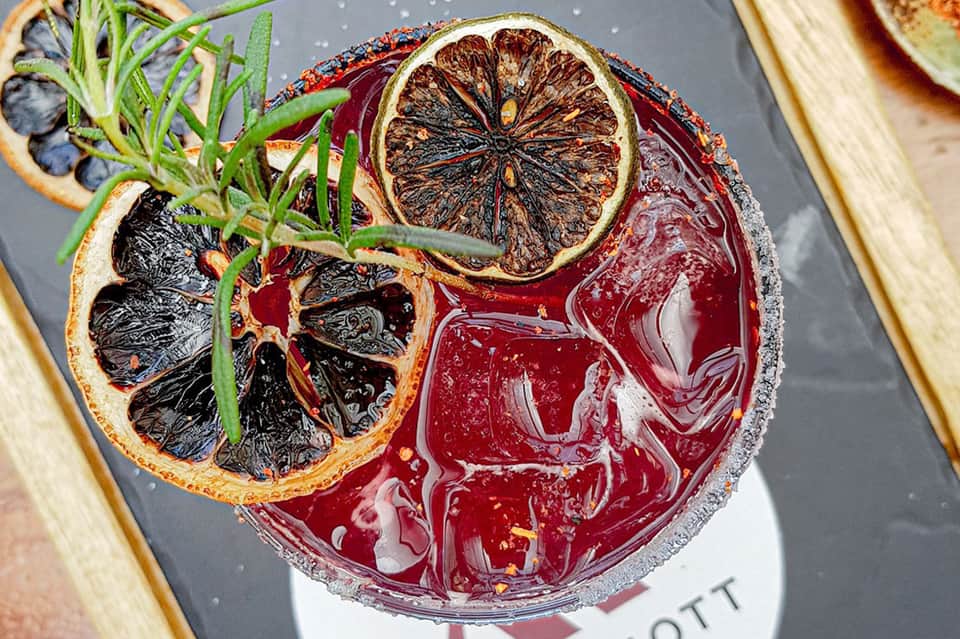 Artistic cocktail with charred lemon slice and rosemary garnish on dark background