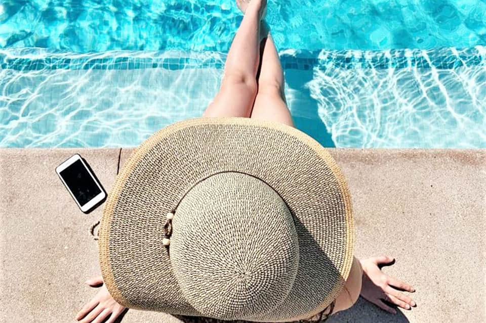 Woman relaxing by swimming pool wearing straw hat with phone nearby