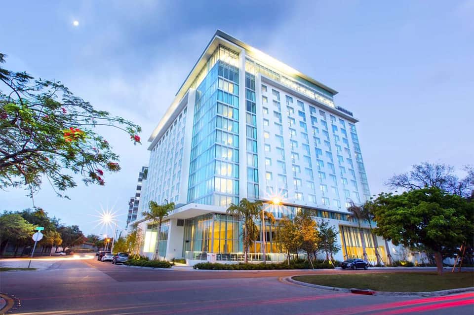 Contemporary hotel building exterior lit at dusk with palm trees and landscaping