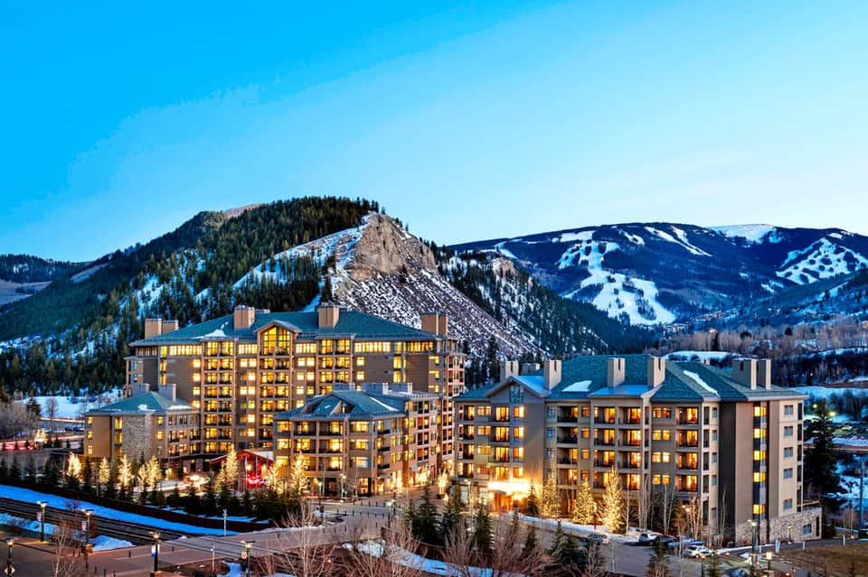 Luxury mountain resort lit up at dusk with ski slopes visible in background