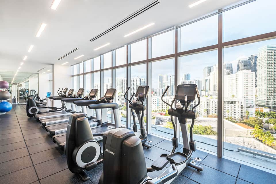 Modern gym with cardio equipment and floor-to-ceiling windows overlooking city skyline