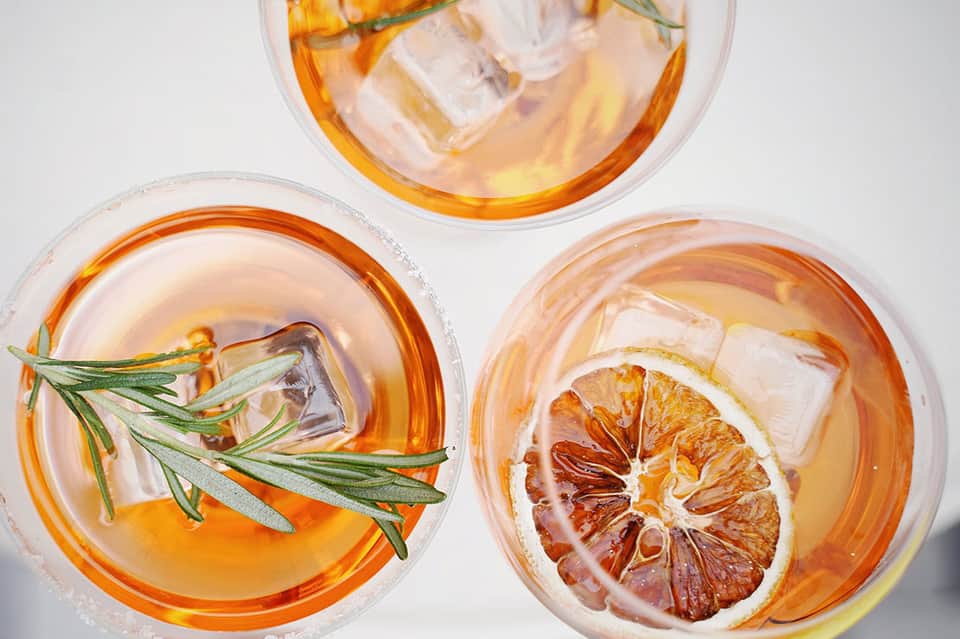 Overhead view of three cocktails with citrus slices, rosemary, and ice in clear glasses