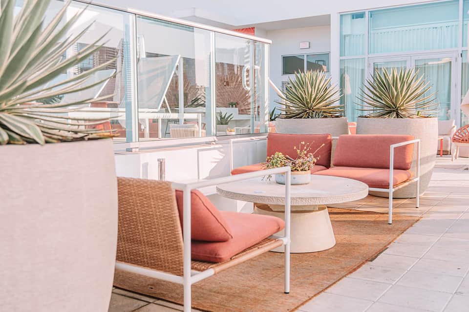 Modern terrace lounge with coral cushioned seating, potted plants, and glass doors