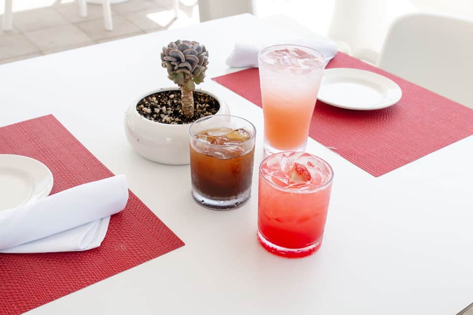 Dining table set with pink napkins, white plates, small potted succulent, and colorful cocktails