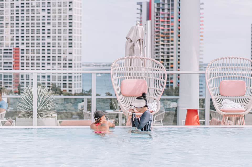 Resort infinity pool with pink hanging chairs overlooking city skyline and water