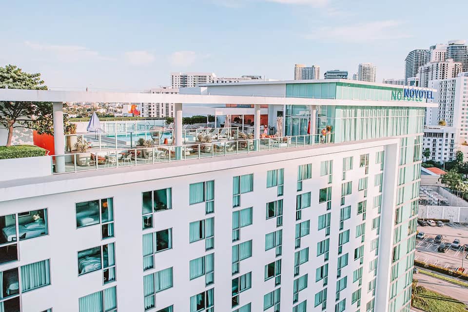 Modern white hotel building with mint-green windows and rooftop restaurant overlooking cityscape and waterfront