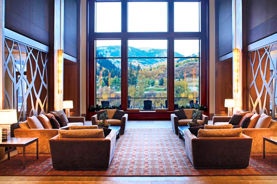 Luxurious lodge lounge with floor-to-ceiling windows overlooking mountain landscape, warm furnishings, and geometric wood panels