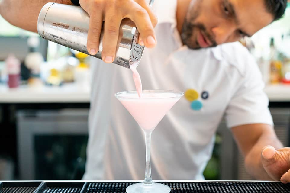 Bartender pouring pink cocktail into martini glass at resort bar