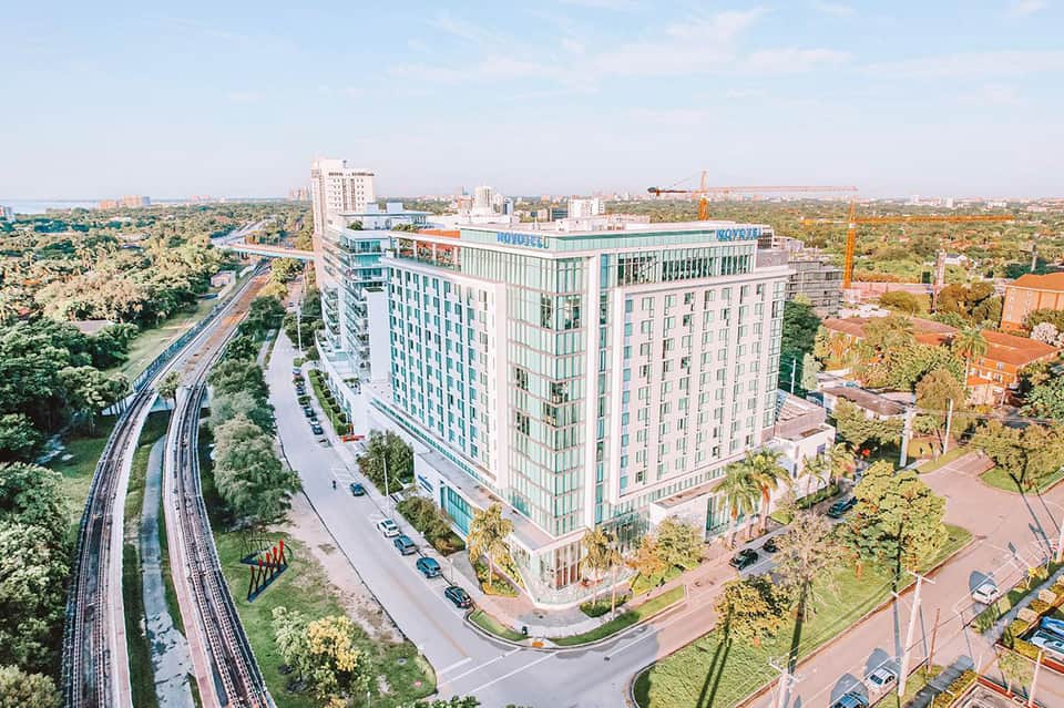 Contemporary hotel exterior with blue and white facade, green landscaping, and curved driveway in urban setting