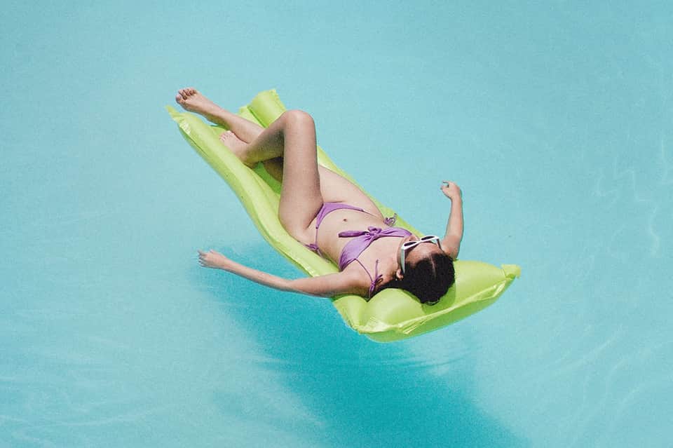 Person relaxing on lime green pool float in bright turquoise resort swimming pool