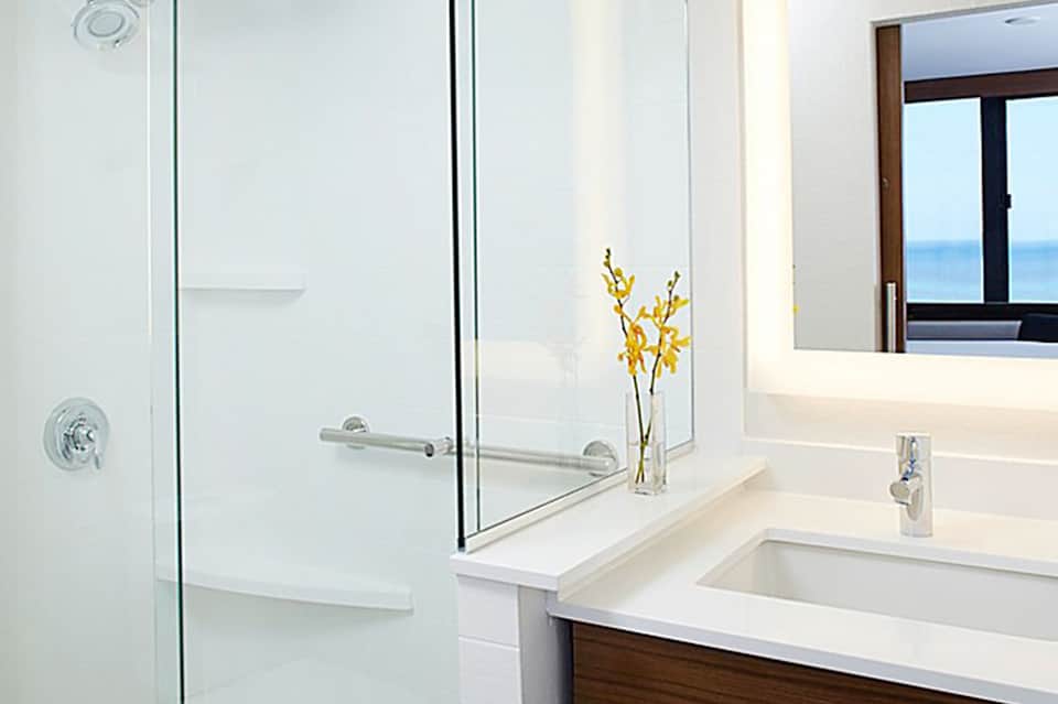 Luxury bathroom with frameless glass shower enclosure, white countertops, vessel sink, and ocean view window