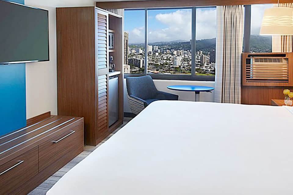 Modern hotel room with city skyline view through floor-to-ceiling windows, wood furnishings, and workspace