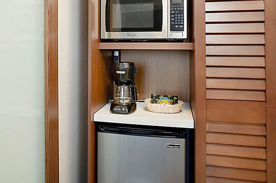 Hotel room kitchenette with microwave, coffee maker, mini refrigerator, and wooden cabinetry