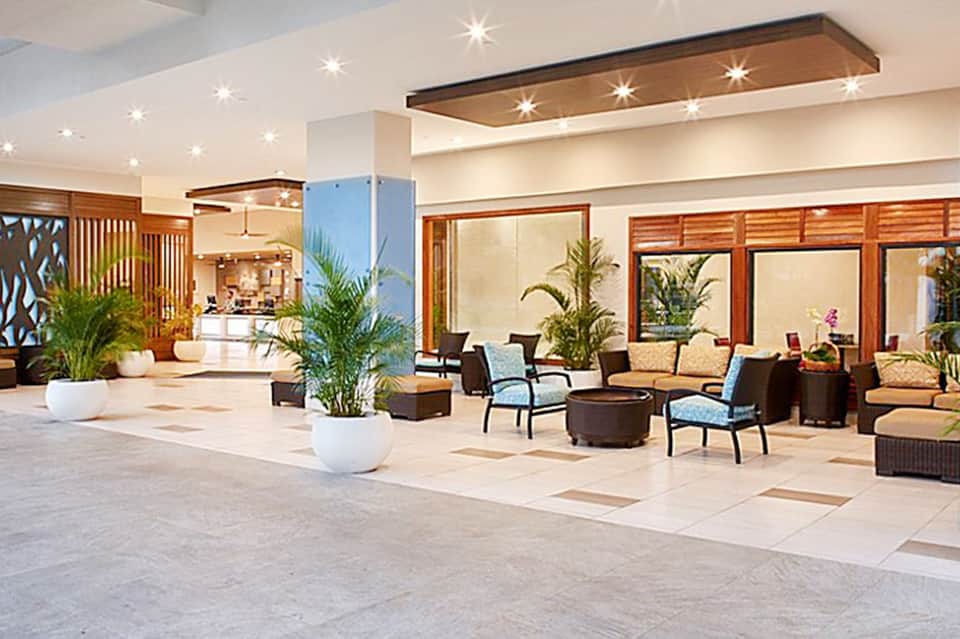 Spacious hotel lobby with recessed ceiling lights, wood paneling, potted plants, and seating areas