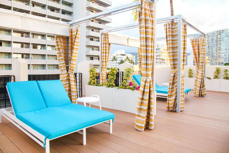 Rooftop deck with bright blue loungers, yellow-striped privacy curtains, and city skyline views