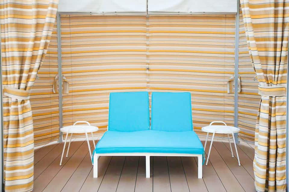 Private cabana with striped canopy, blue cushioned seating, and side tables
