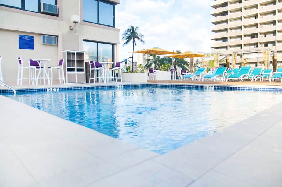 Resort pool with turquoise water, lounge chairs, palm tree, and high-rise buildings