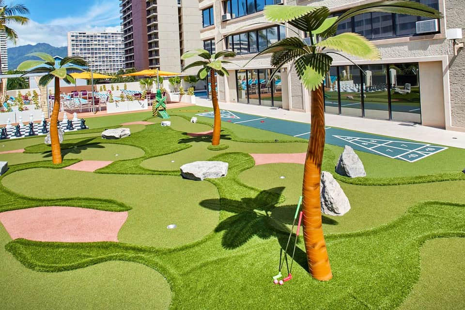 Miniature golf course with palm trees and colorful fairways at a resort with high-rise buildings