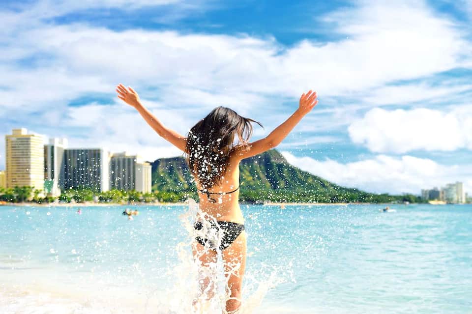 Child running into turquoise ocean water with palm-lined beach and high-rise hotels in background