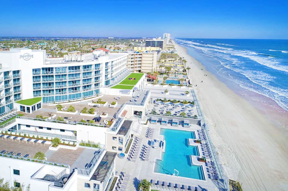 Beachfront resort aerial view with pools, terraces, palm trees, and sandy beach with ocean