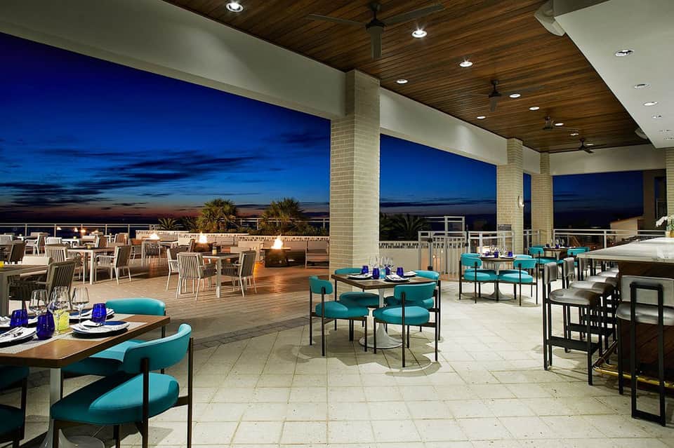 Modern rooftop dining area with turquoise chairs, tables, and panoramic evening sky views
