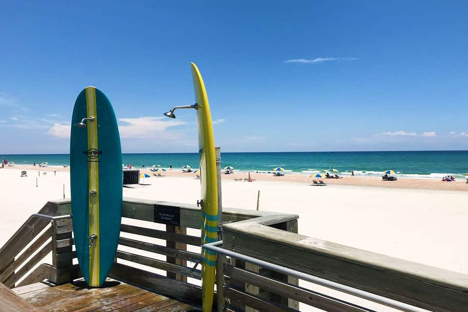 Two teal and yellow surfboards mounted on wooden beach boardwalk railing overlooking sandy beach and ocean
