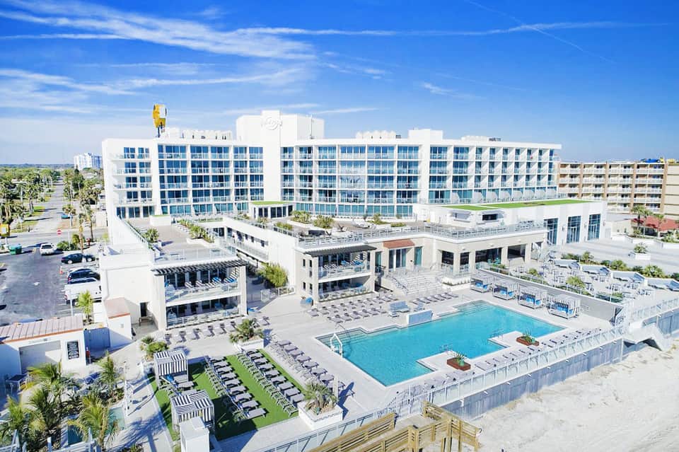 Beachfront hotel with white building, turquoise pool, lounge chairs, and sandy beach access
