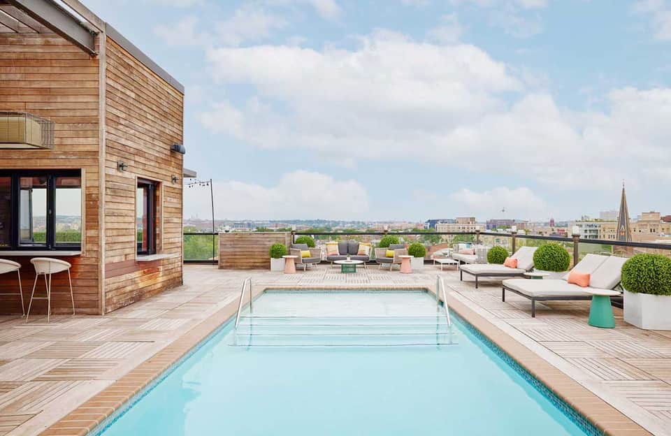 Modern rooftop pool deck with wooden loungers, city skyline views, and wood-clad building