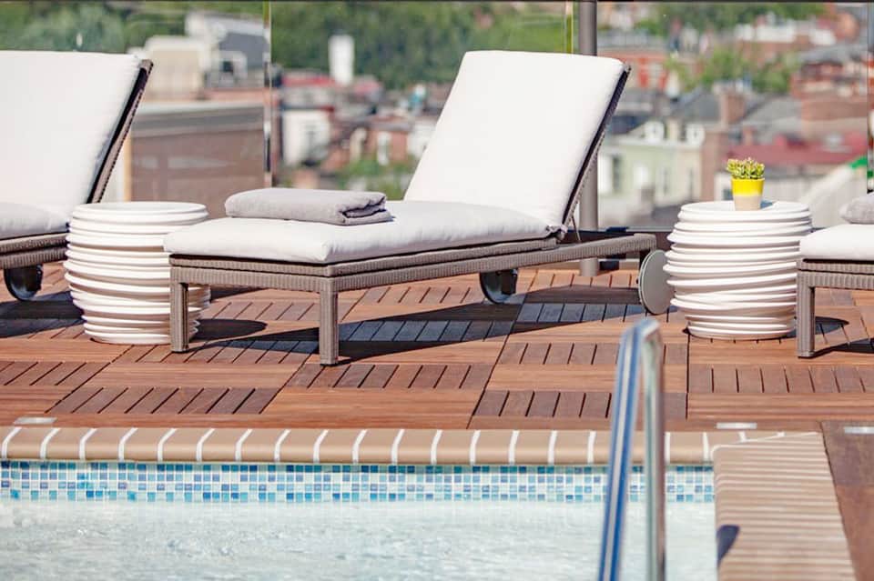 Wooden deck with white lounge chairs and small tables overlooking hotel pool