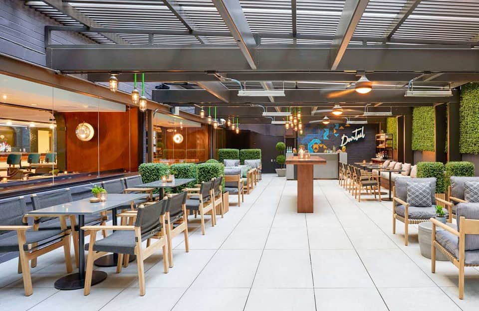 Contemporary hotel terrace with wooden tables, chairs, hanging lights, and glass storefront