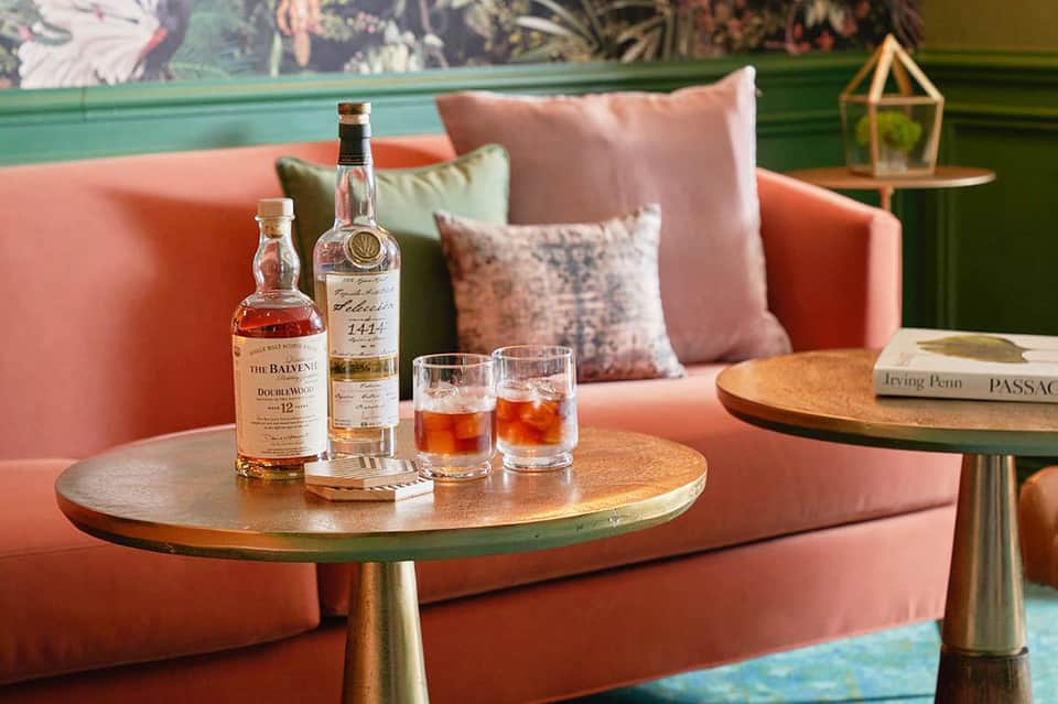 Luxury lounge with coral velvet sofa, decorative pillows, whiskey bottles, and jewel-tone accents
