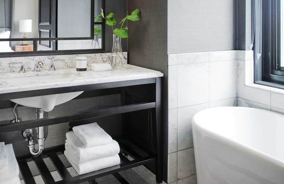Contemporary bathroom with black vanity, marble countertop, white soaking tub, and large mirror