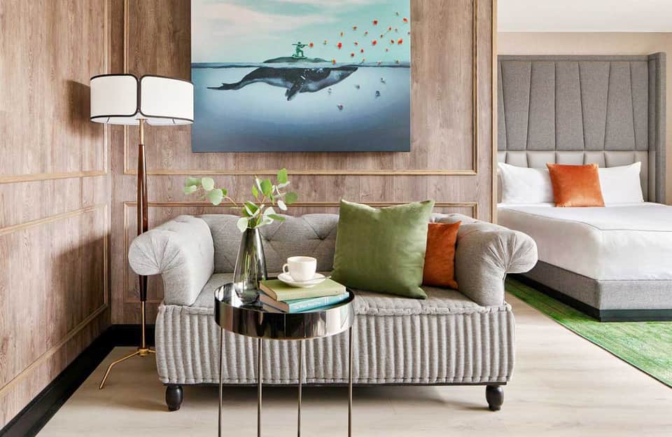 Contemporary hotel suite with sofa, whale artwork, green accents, and bedroom visible in background